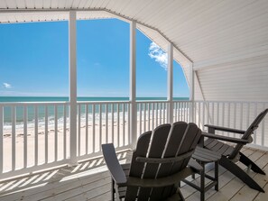 A covered deck with two Adirondack chairs facing a beach.