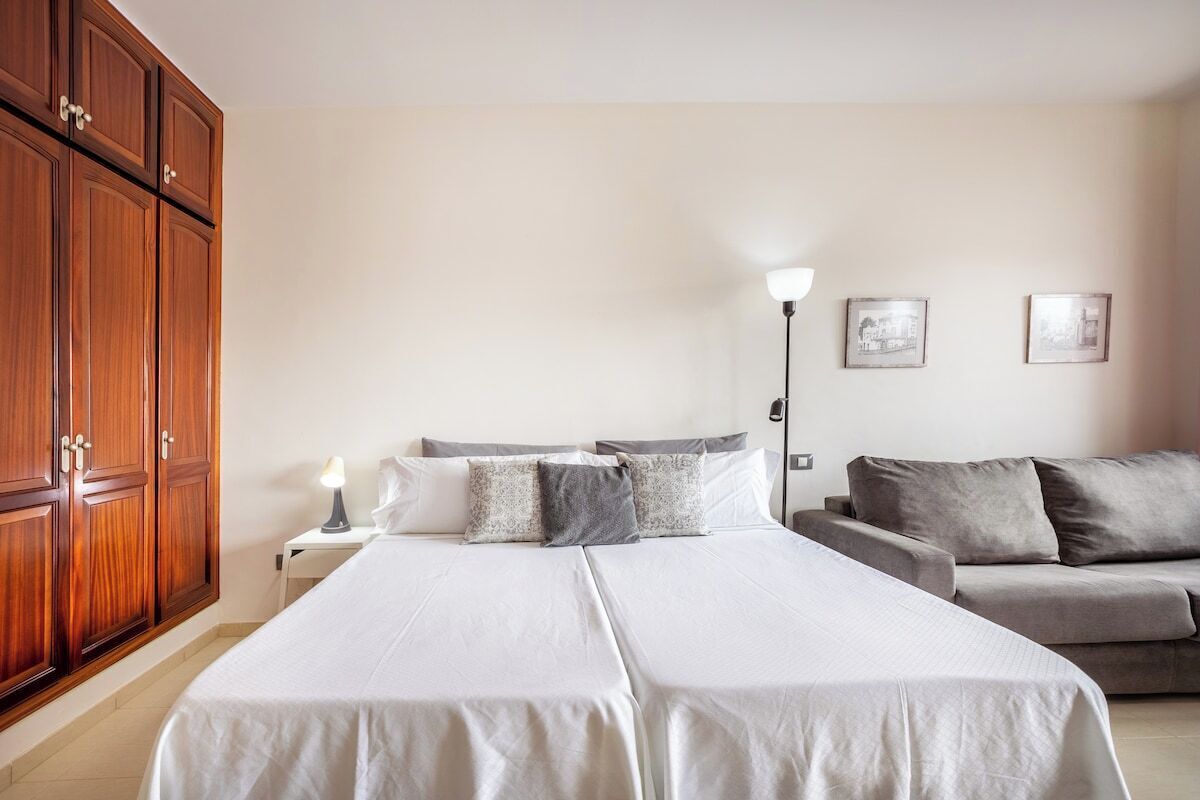 Une chambre d’hôtel avec deux lits, un canapé, une armoire en bois, des lampes de chevet et des tableaux encadrés au mur.