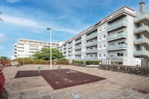 A residential building with multiple balconies, a playground with swings, and a paved courtyard.