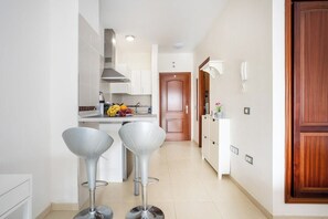 A modern kitchen with white cabinets, a stainless steel range hood, and two bar stools.