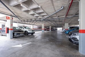 Un parking souterrain où sont garées plusieurs voitures, avec des piliers en béton et des flèches directionnelles peintes sur le sol.