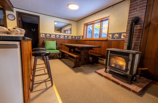 A cozy kitchen with a wood-burning stove, a wooden table, and a green chair. - Spacious Chalet, Skiing 5 Minutes to Jay Peak, Vermont! (Montgomery)