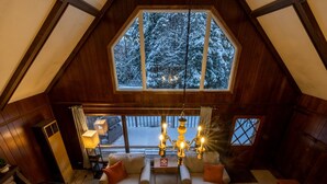 A cozy loft bedroom with a large skylight, wooden beams, a chandelier, and a view of snow-covered trees. - Spacious Chalet, Skiing 5 Minutes to Jay Peak, Vermont! (Montgomery)