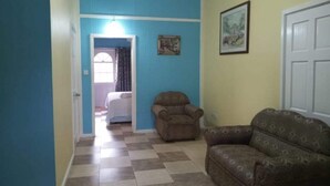 Un salon avec un canapé à motifs, un fauteuil et une porte donnant sur une autre pièce.