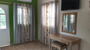 Une pièce comprenant un bureau en bois, une chaise, un téléviseur fixé au mur et une fenêtre avec des rideaux.