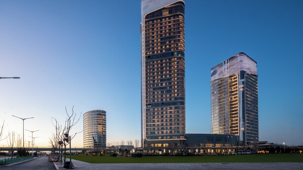 A modern hotel with a prominent curved facade, multiple floors, and a clear sky in the background.
