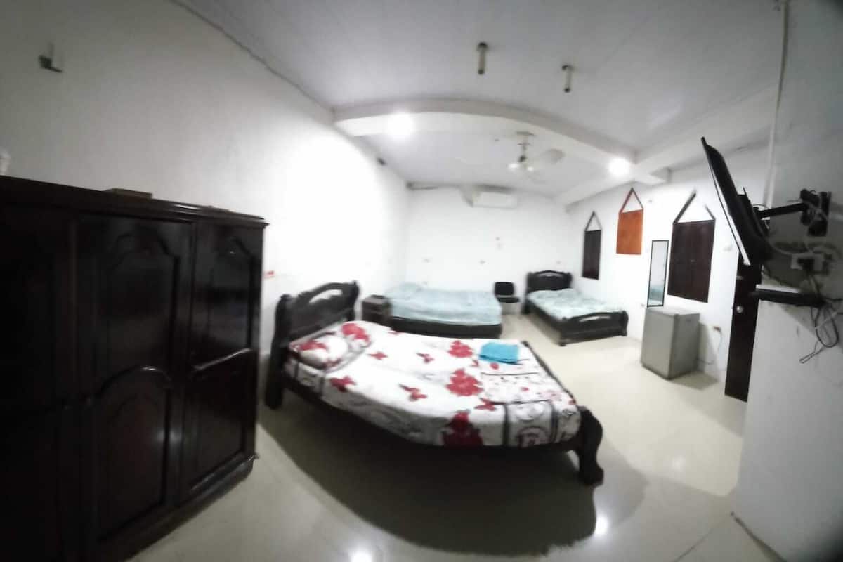 A bedroom with a large wardrobe, two single beds, a small table, and a TV mounted on the wall.