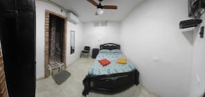 Una habitación pequeña y estrecha con una cama individual, un ventilador de techo y una puerta que da a otra habitación.