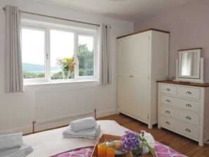 Une chambre à coucher avec un lit, une commode, une fenêtre avec des rideaux, un radiateur et une vue sur la verdure à l’extérieur.