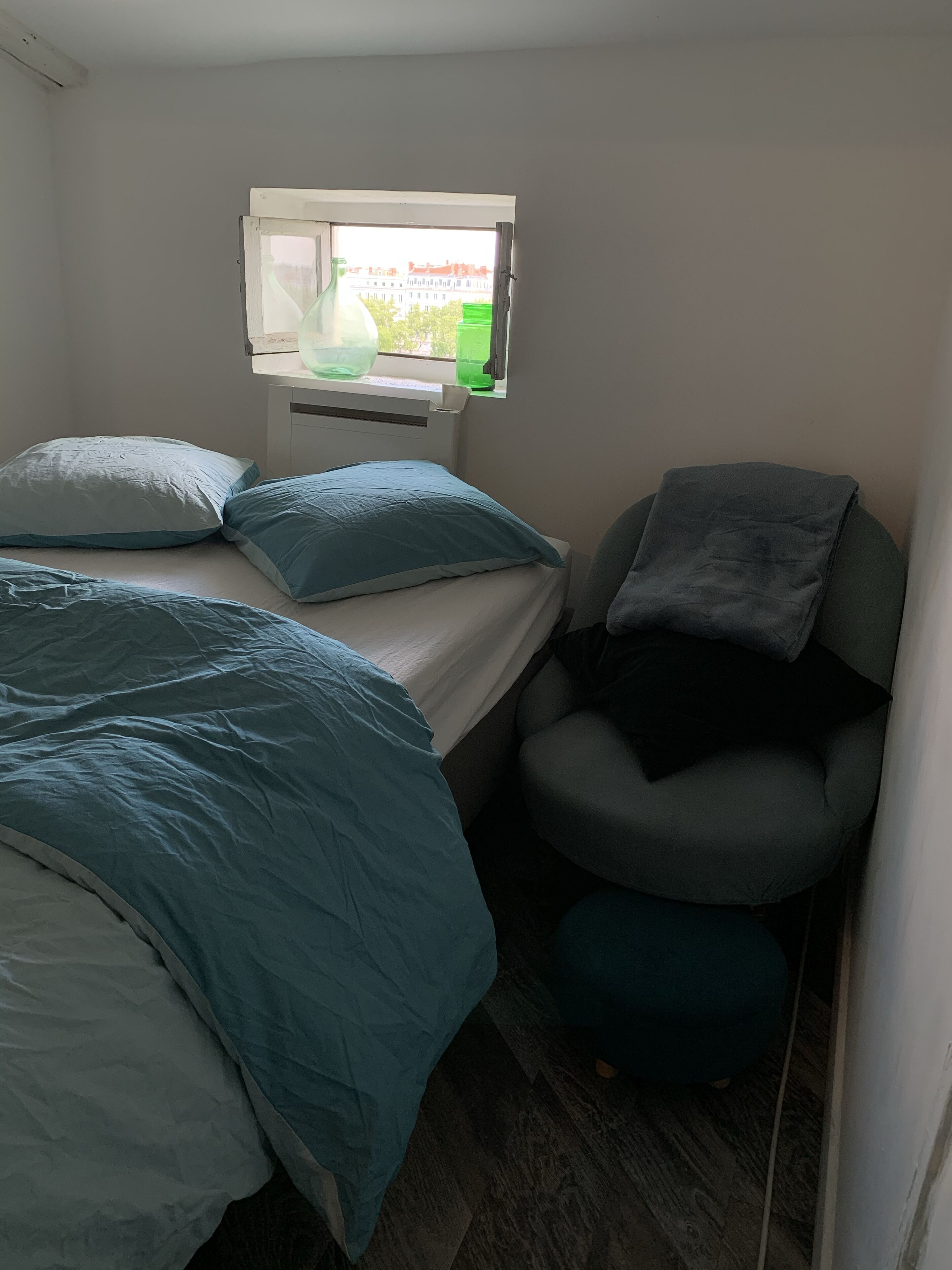 A small, compact room with two beds, a window, and a chair.