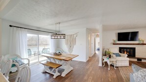 Ein geräumiges Wohnzimmer mit Holzboden, Kamin, Wandfernseher und Essbereich inklusive Tisch und Stühlen.