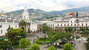 A historic plaza with a prominent white building featuring a bell tower, surrounded by lush greenery and a flag. - Lovely 2-Bedroom Rental Unit in Quito (QUITO)