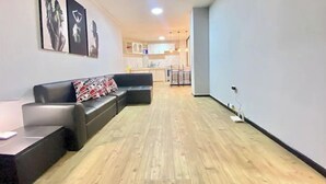 A modern living room with a black leather sofa, a wooden floor, and a kitchen in the background. - Lovely 2-Bedroom Rental Unit in Quito (QUITO)