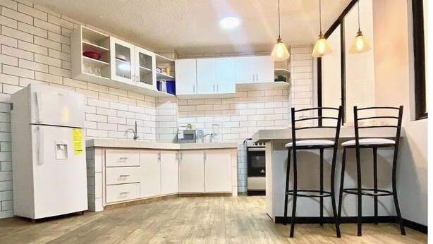 A kitchen with white cabinets, a built-in oven, and a bar area with two black chairs. - Lovely 2-Bedroom Rental Unit in Quito (QUITO)