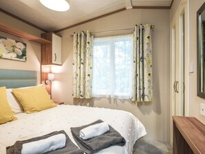 A bedroom with a bed, pillows, a nightstand, a lamp, a window with curtains, and a door.