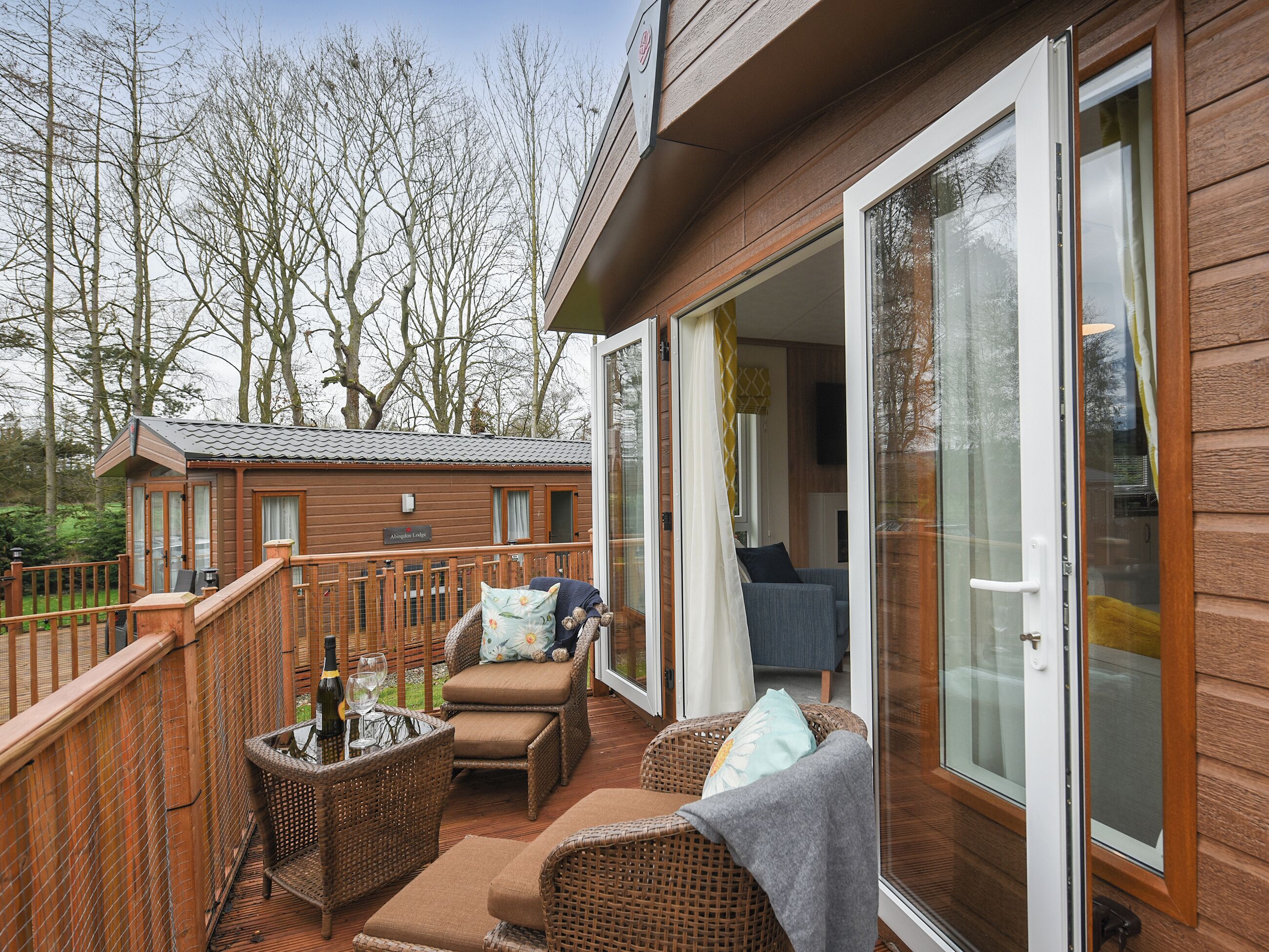 Une terrasse en bois avec des meubles en osier, une bouteille de vin et un verre.