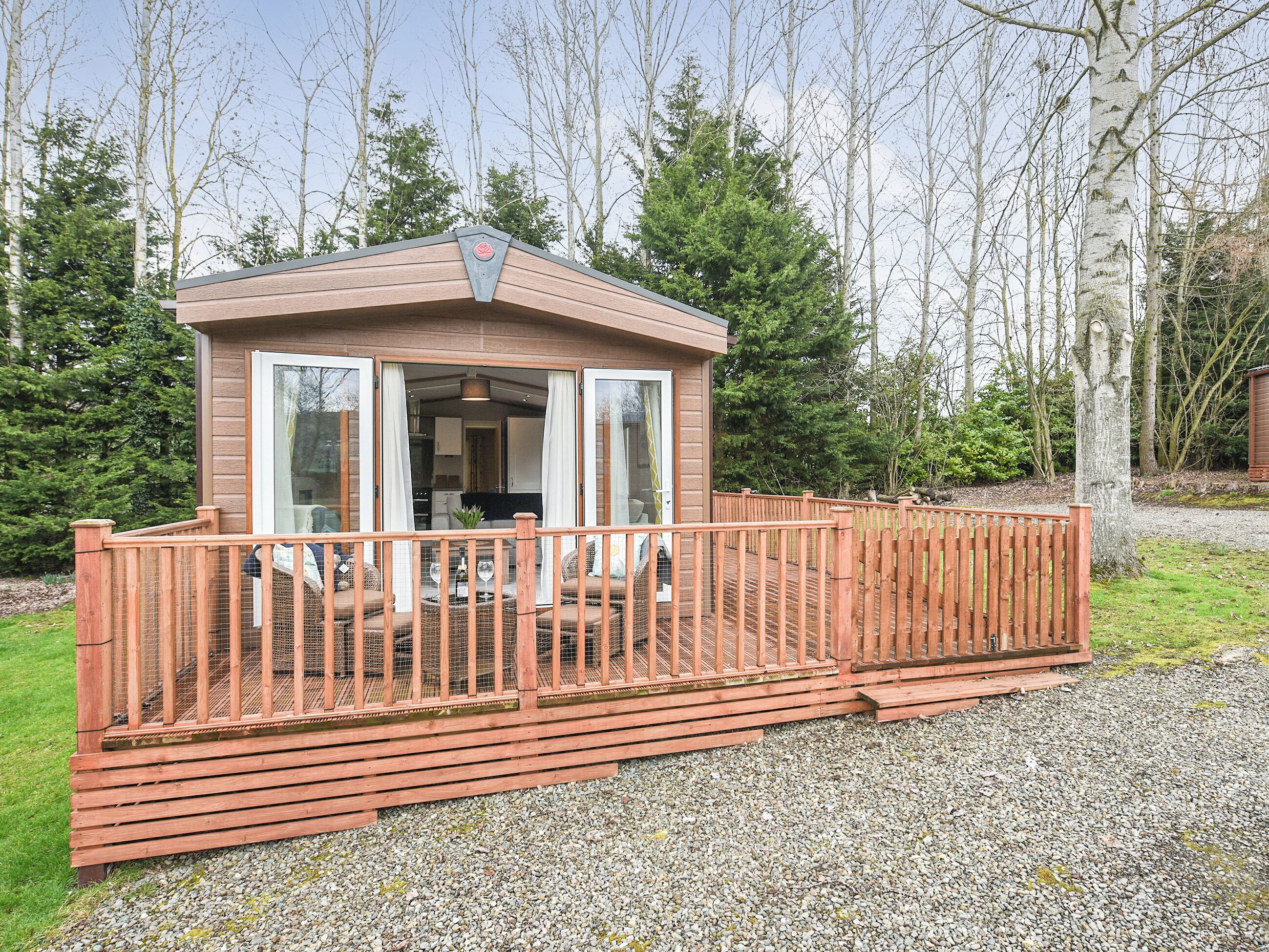 A wooden cabin with a deck, a glass door, and a small kitchen visible inside.