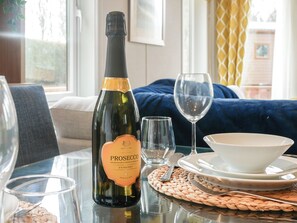 Uma garrafa de vinho Prosecco, uma taça, uma tigela e um prato sobre uma mesa com um jogo americano trançado.