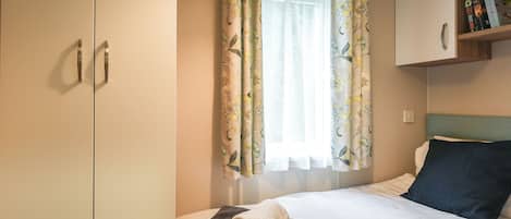 A hotel room with a bed, a wardrobe, a window with floral curtains, and a bookshelf with books.