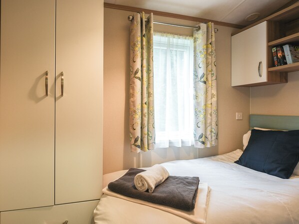 A hotel room with a bed, a wardrobe, a window with floral curtains, and a bookshelf with books.
