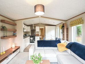 A modern living room with a sofa, a coffee table with flowers, and a kitchen in the background.