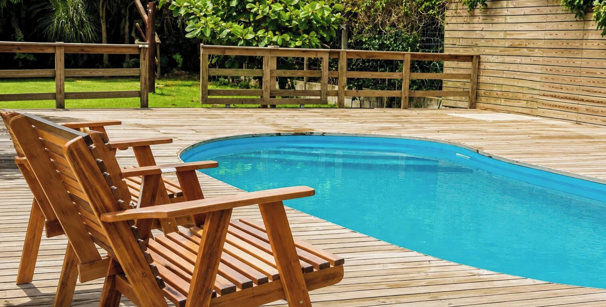 A wooden deck with a swimming pool, surrounded by a wooden fence and greenery.