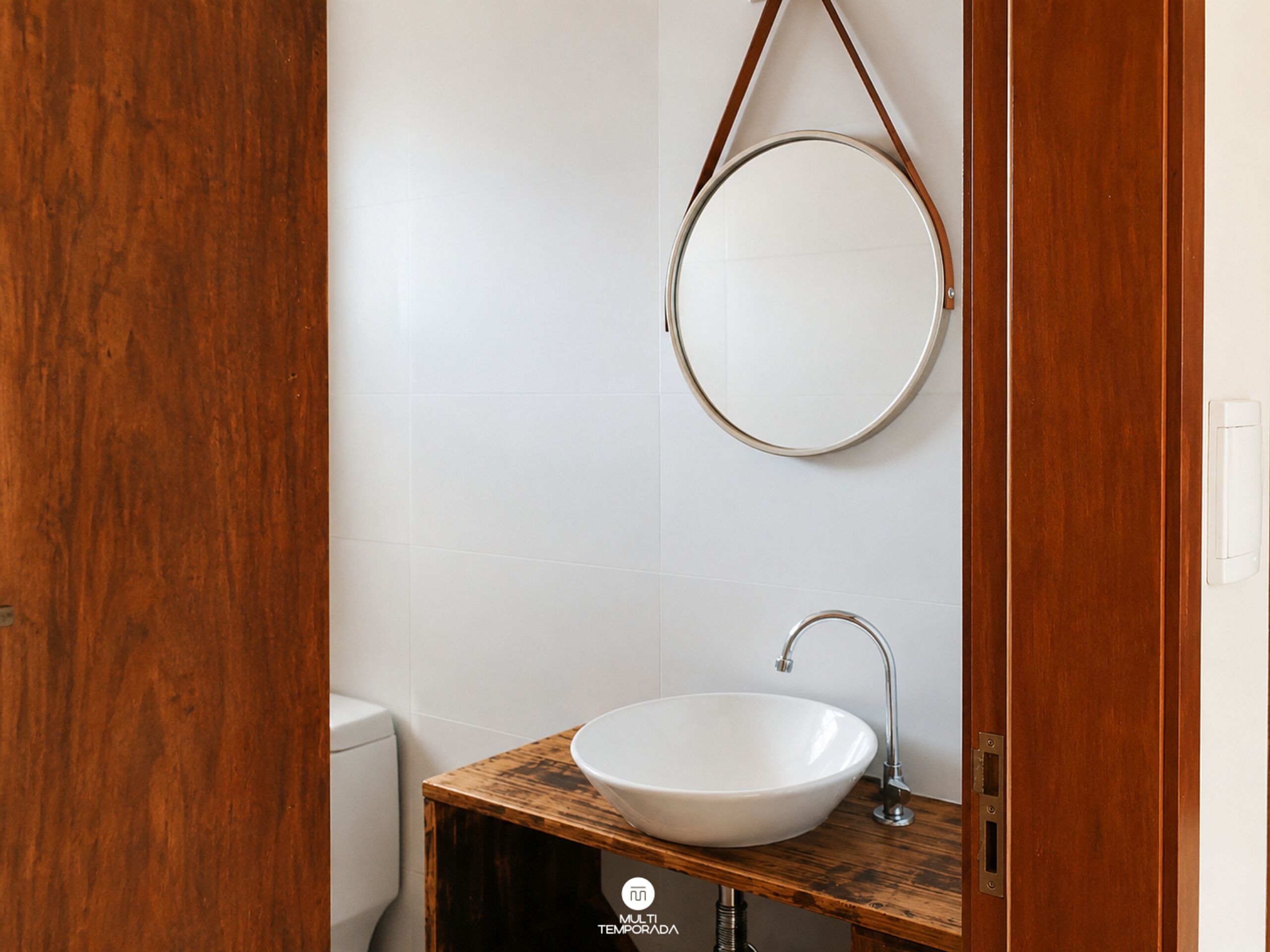 Une salle de bain avec un meuble-lavabo en bois, un lavabo blanc et un miroir rond.