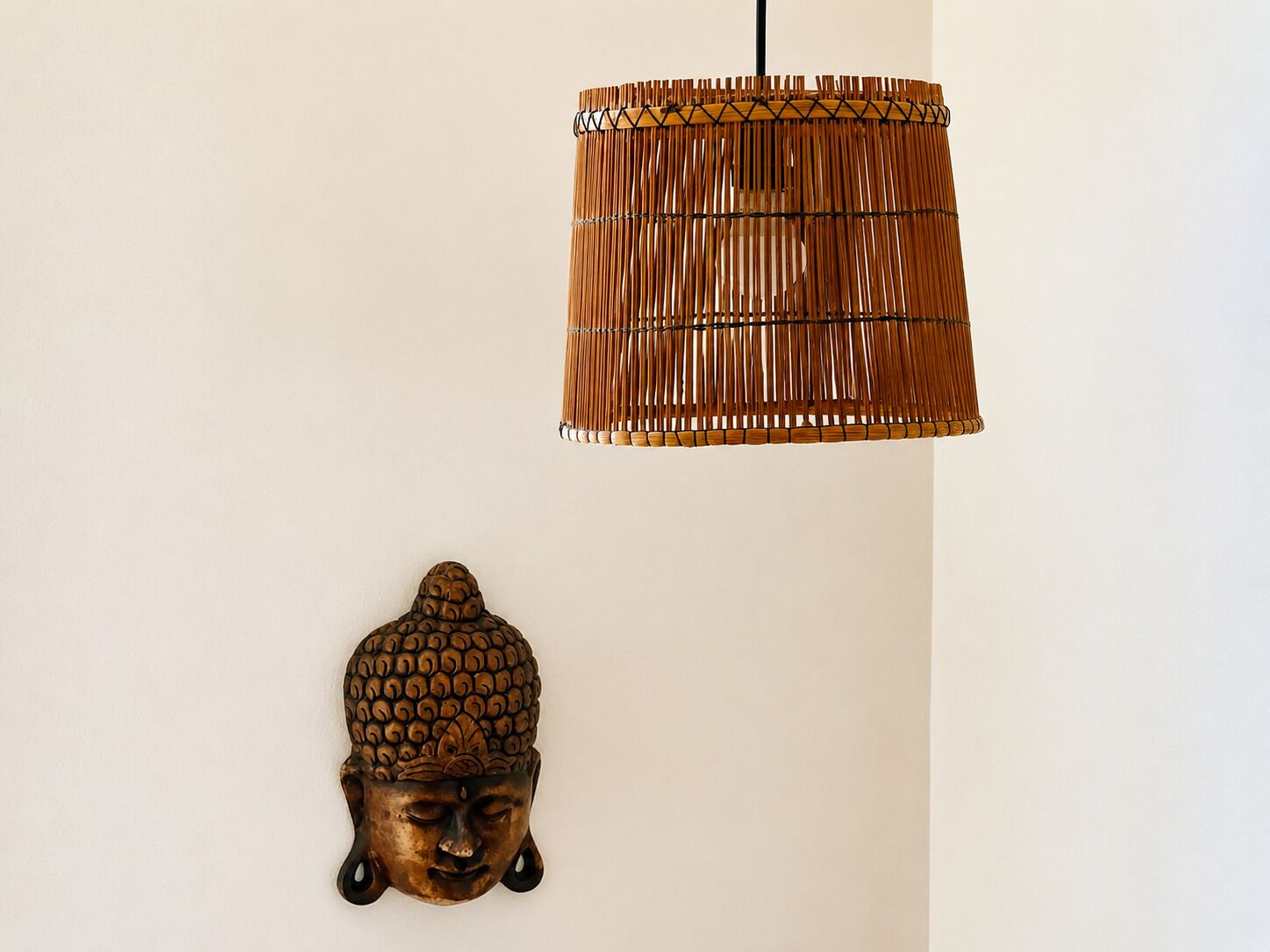 A wall-mounted lamp with a woven shade and a decorative Buddha head sculpture.