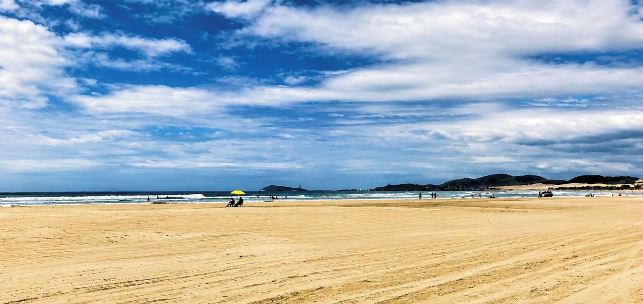A wide sandy beach with a clear sky and distant hills.