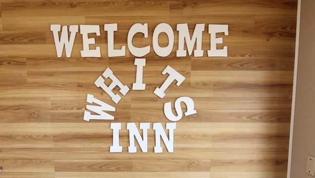 A wooden wall with the text "WELCOME WHITS INN" in white letters.