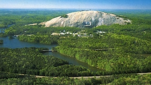 A large hill with a small building on top, surrounded by dense forest and a river.