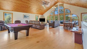 A spacious living area with a pool table, comfortable seating, and large windows offering natural light and views. - Angel Bear Chalet- Private Lake/Beach/Sauna/Hot Tub/Gym/Firepit/Float Trampoline (Peru)