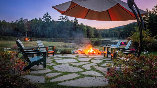 An outdoor patio with stone flooring, two Adirondack chairs, a table, and a large umbrella. - Angel Bear Chalet- Private Lake/Beach/Sauna/Hot Tub/Gym/Firepit/Float Trampoline (Peru)