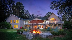 A two-story house with a fire pit in the front yard, a covered patio, and a large window overlooking the yard. - Angel Bear Chalet- Private Lake/Beach/Sauna/Hot Tub/Gym/Firepit/Float Trampoline (Peru)