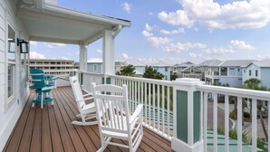 A wooden deck with white railings and rocking chairs, overlooking a row of houses.