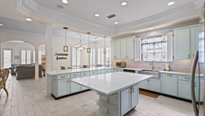 A spacious kitchen with light blue cabinets, a large island, and pendant lighting.