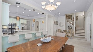 A spacious kitchen with white cabinets, a wooden dining table, and a chandelier.