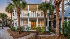 A two-story building with a balcony, palm trees, and a pathway leading to the entrance.