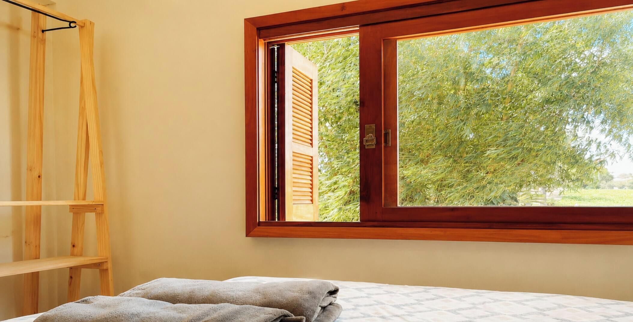 Een kamer met een bed, een houten plank en een raam met uitzicht op bomen.