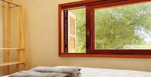 Una habitación con una cama, un estante de madera y una ventana con vistas a árboles.