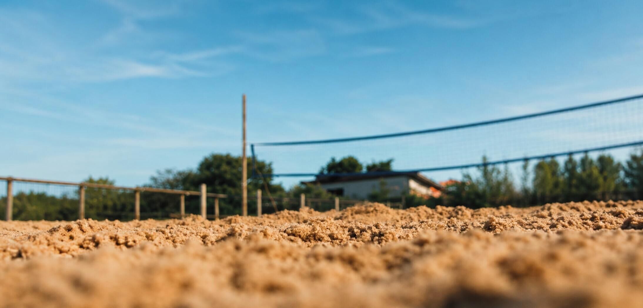 Una cancha de voleibol con una red, rodeada por una cerca y árboles al fondo.