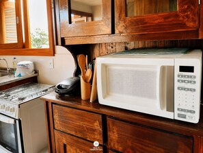 A kitchen with a microwave, stove, and wooden cabinets. - Rosa Pantai Beach Village (Imbituba)