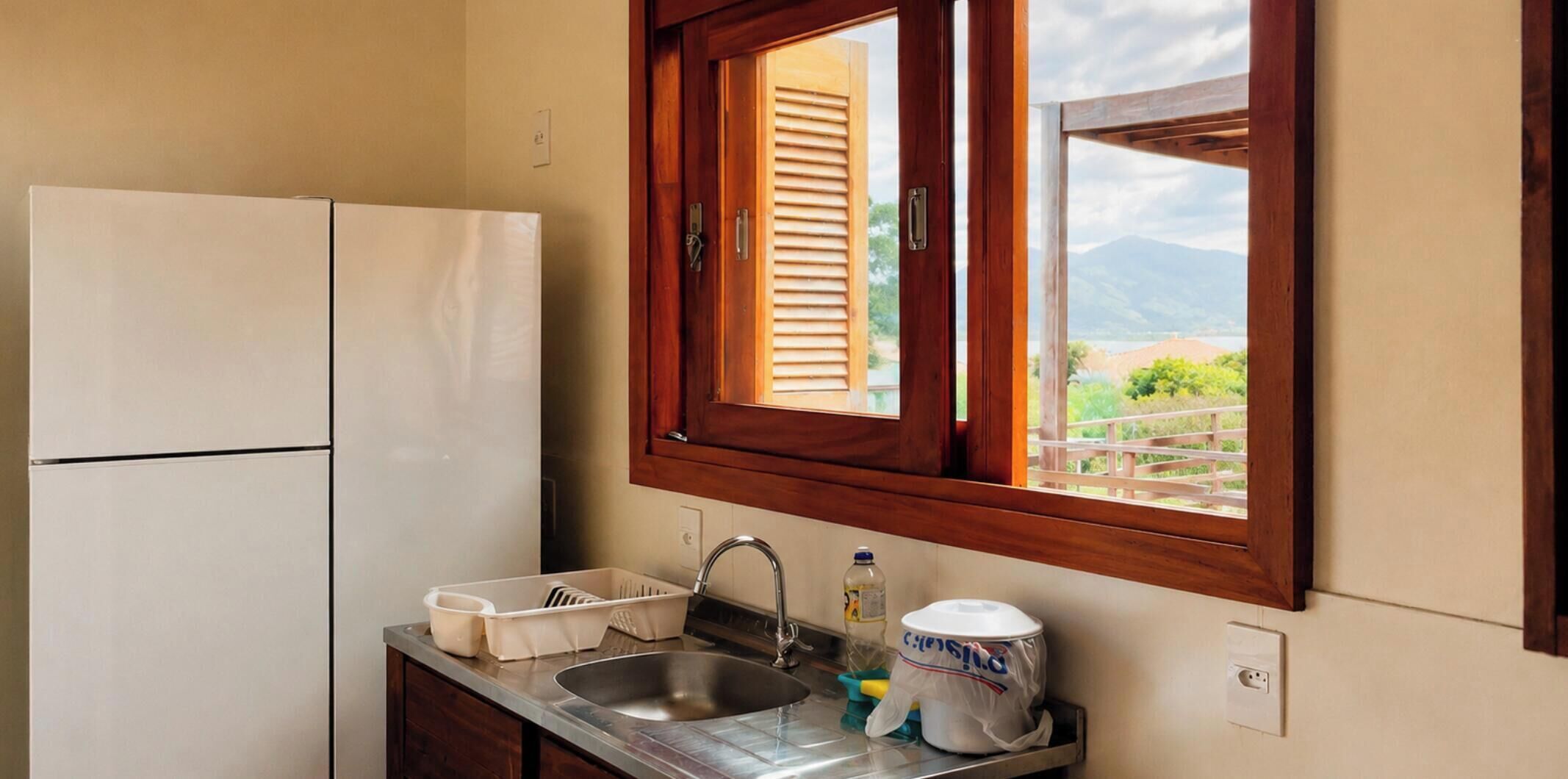 A compact kitchen with a built-in refrigerator, a sink with a dish rack, and a window with wooden shutters.