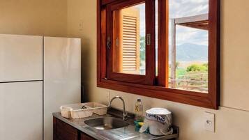 A compact kitchen with a built-in refrigerator, a sink with a dish rack, and a window with wooden shutters.