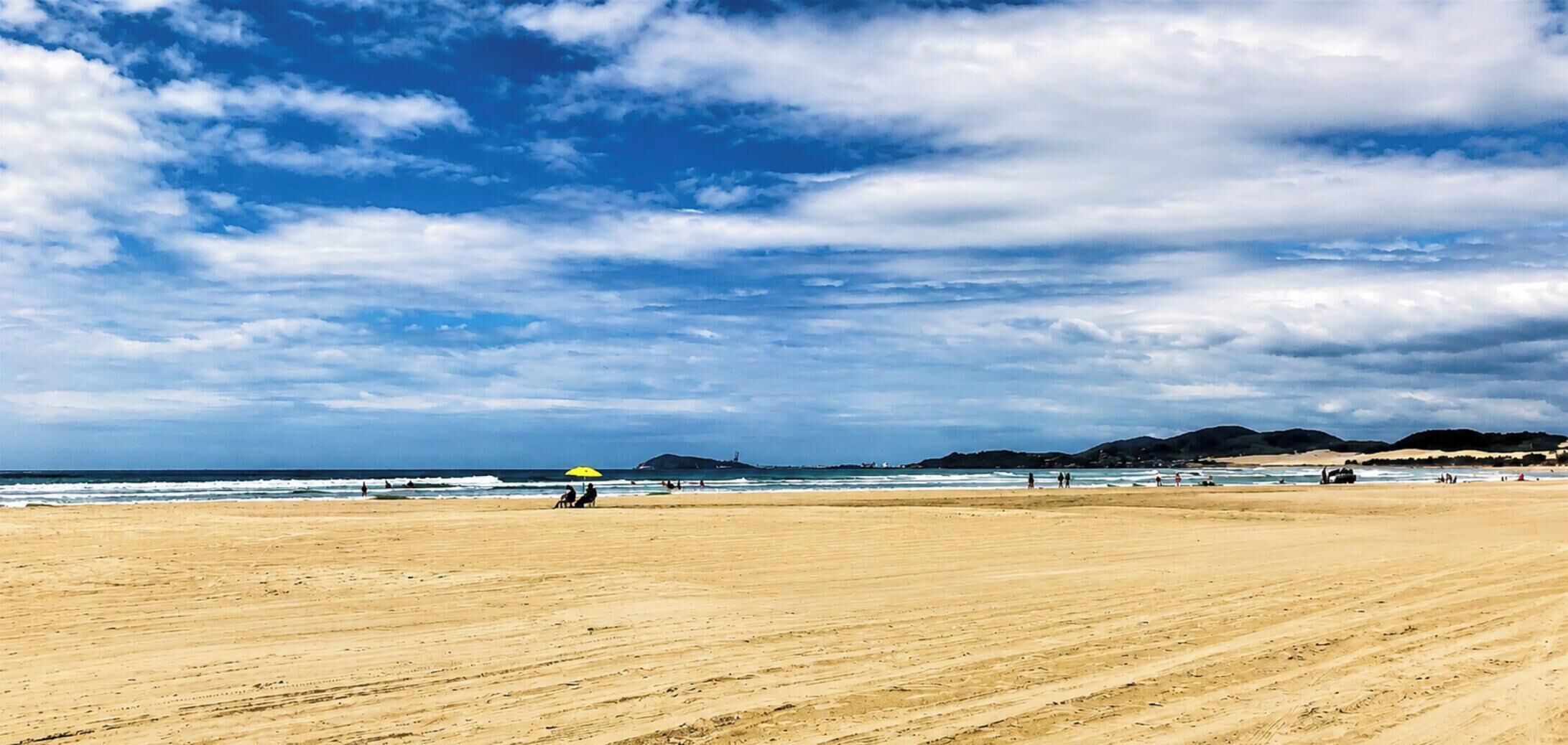 Una extensa playa arenosa con cielo despejado y colinas a lo lejos.