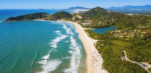 Vista aérea de una zona costera con playa, aguas azules cristalinas y un promontorio cubierto de bosque.