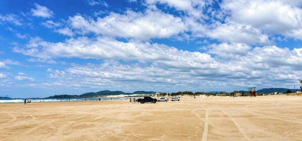 Una playa amplia de arena, cielo despejado y montañas a lo lejos.
