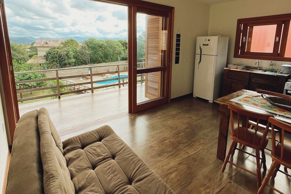 A spacious living area with a large window, a sofa, a dining table, and a kitchen area.