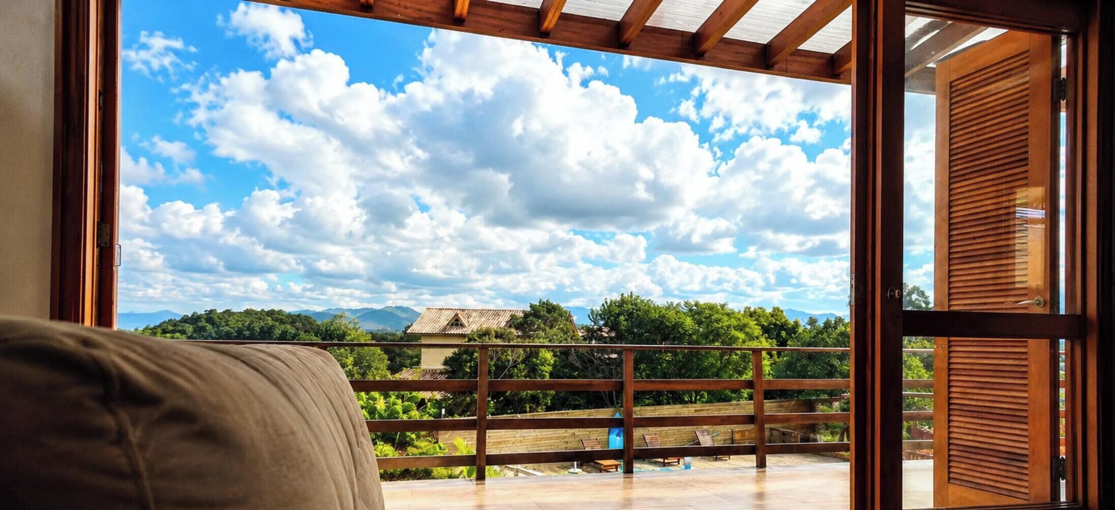 Une pièce dotée d’une grande fenêtre donnant sur un balcon, d’où l’on peut admirer une maison et la verdure environnante.