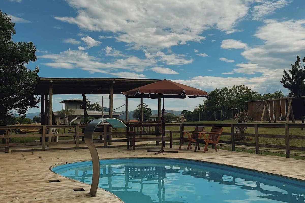 A wooden deck surrounding a swimming pool with a covered seating area and a clear sky.